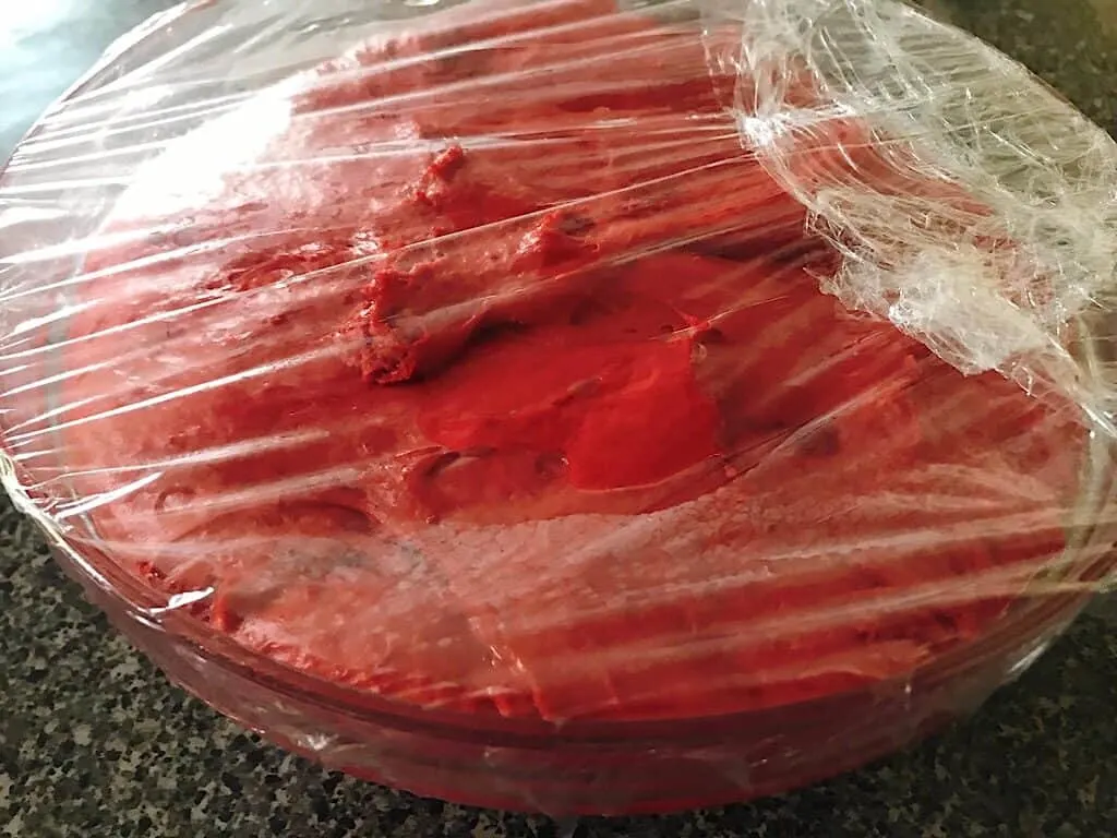 Red Velvet Cinnamon Roll dough in a bowl covered with plastic wrap.