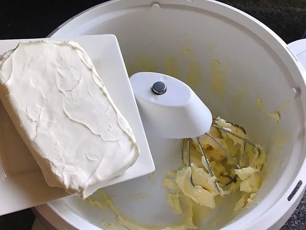 A block of cream cheese over the bowl of a stand mixer to make cream cheese butter cream frosting