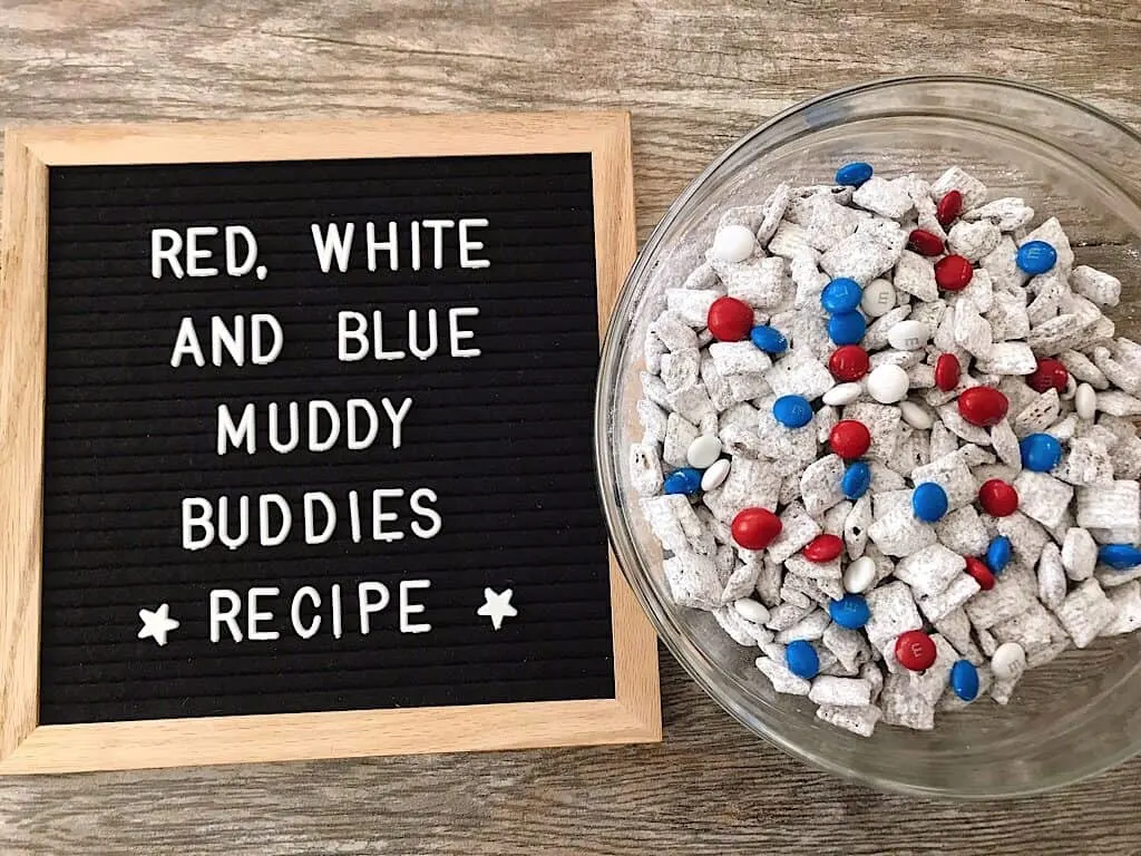 A bowl of Muddy Buddies with Red, White, and Blue M&M’s for the 4th of July and a Letter board sign that says “Red White and Blue Muddy Buddies Recipe”.