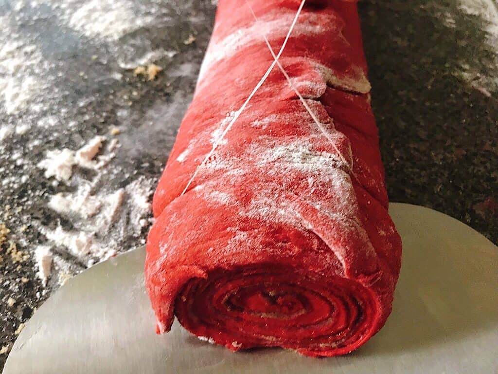 A roll of red velvet cinnamon rolls being cut with dental floss