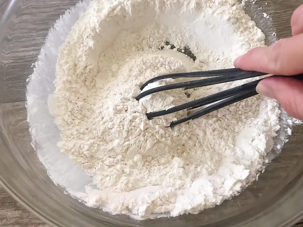 A whisk mixing dry ingredients to make crispy waffle batter.