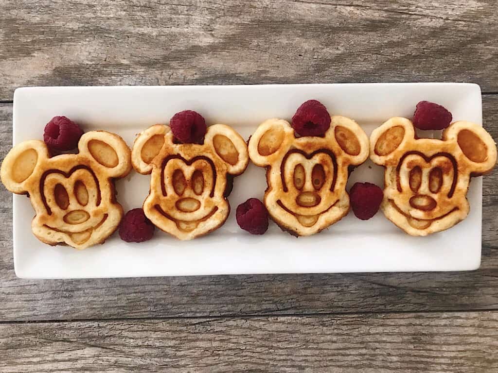 Gofres crujientes con forma de Mickey Mouse alineados en un plato blanco con frambuesas.
