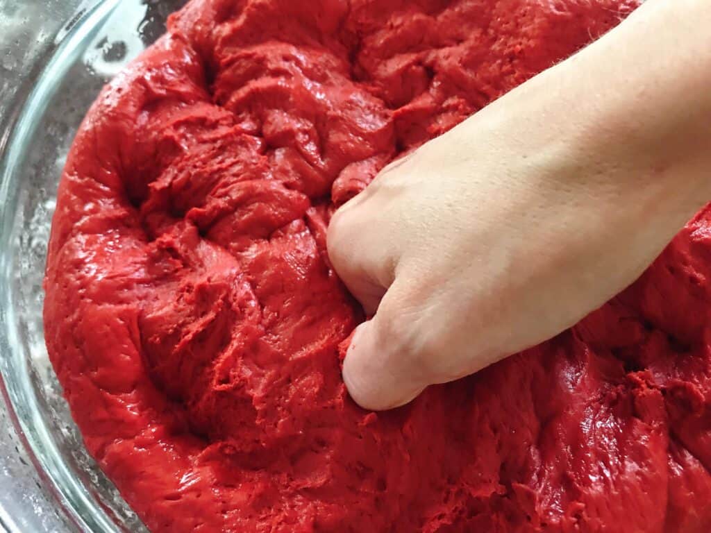 A hand punching down red velvet cake mix cinnamon roll dough