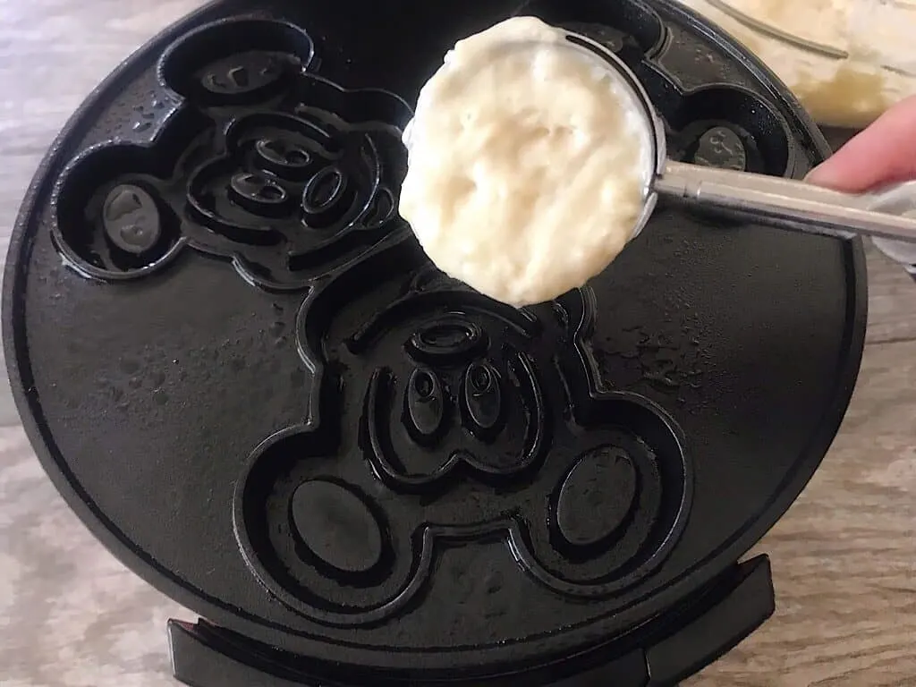 A scoop of crispy waffle batter over a Mickey waffle iron.