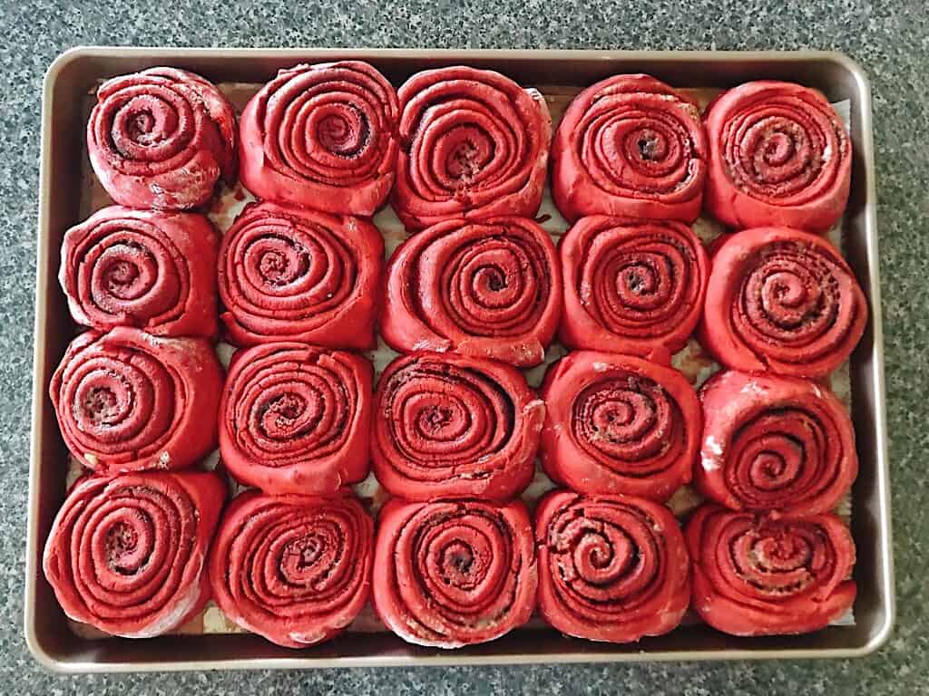 Freshly baked red velvet cinnamon rolls on a baking sheet.