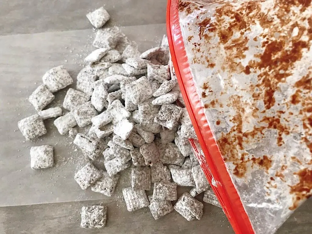 Muddy Buddies covered in powdered sugar being poured out of a ziplock bag.