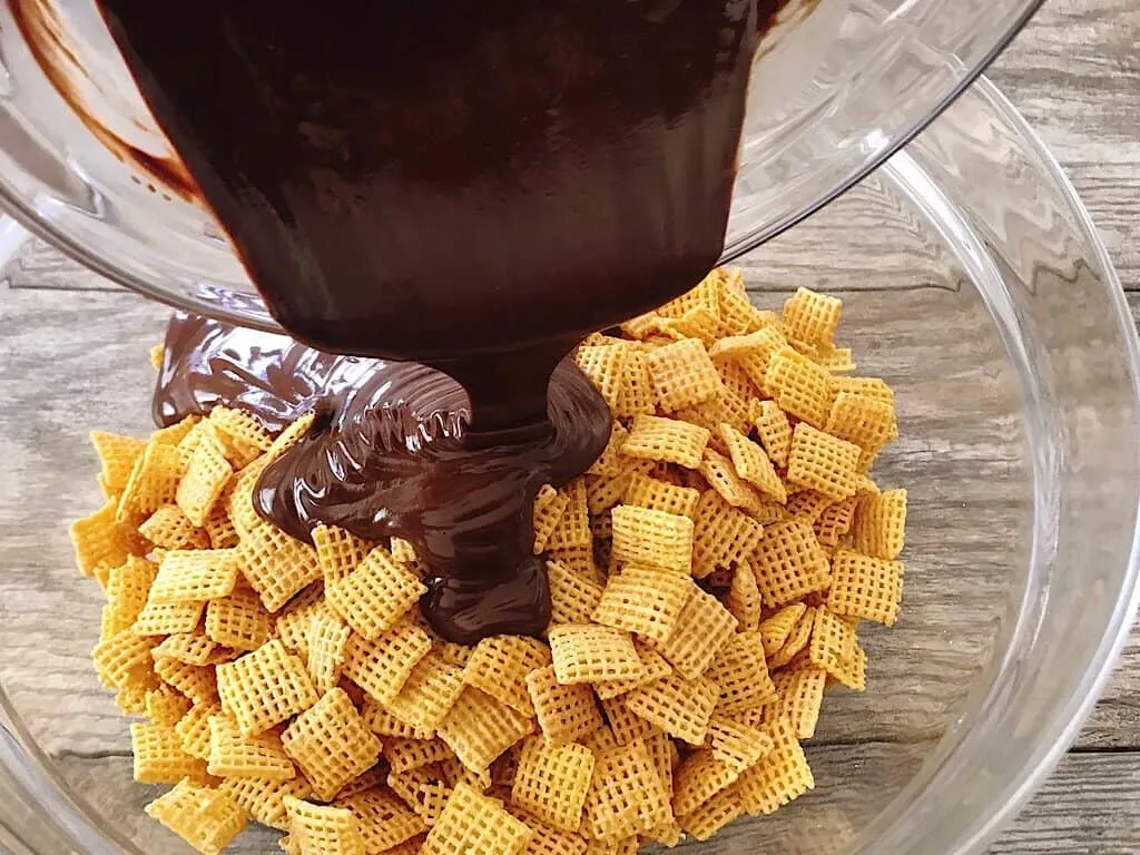 Melted chocolate being poured over a bowl of Chex cereal to make Muddy Buddies Recipe.