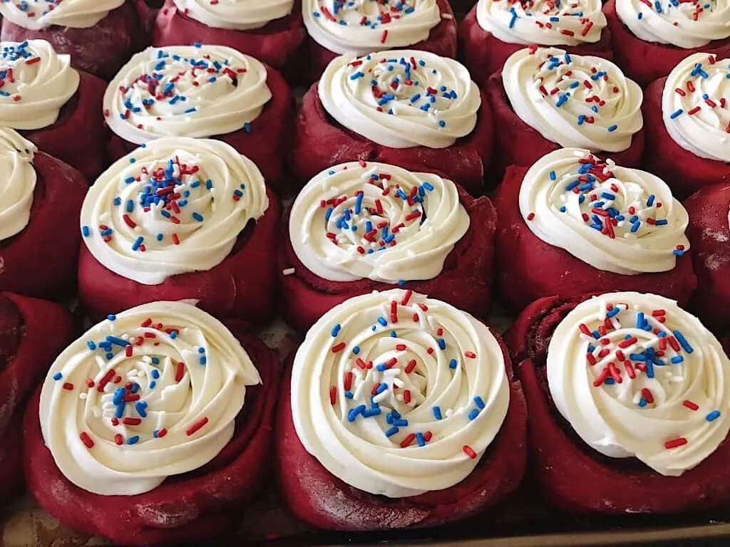 A pan of red velvet cake mix cinnamon rolls with cream cheese frosting with red, white, and blue sprinkles for the 4th of July breakfast.