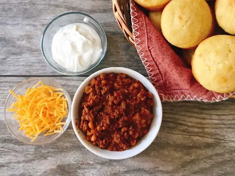 A bowl of Buffalo Chicken Chili with cornbread muffins and toppings.
