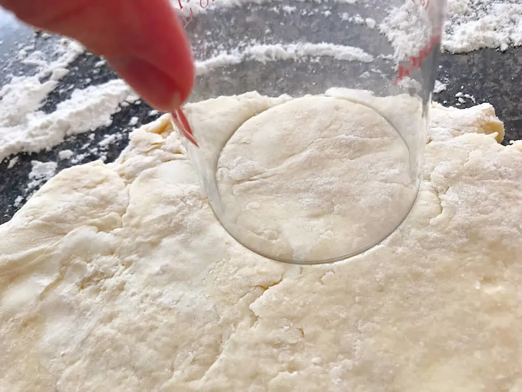 A cup cutting a biscuit out of dough