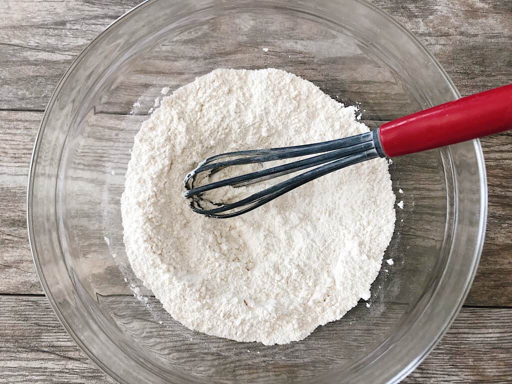 A whisk and dry ingredients to make Honey Buttermilk Biscuits