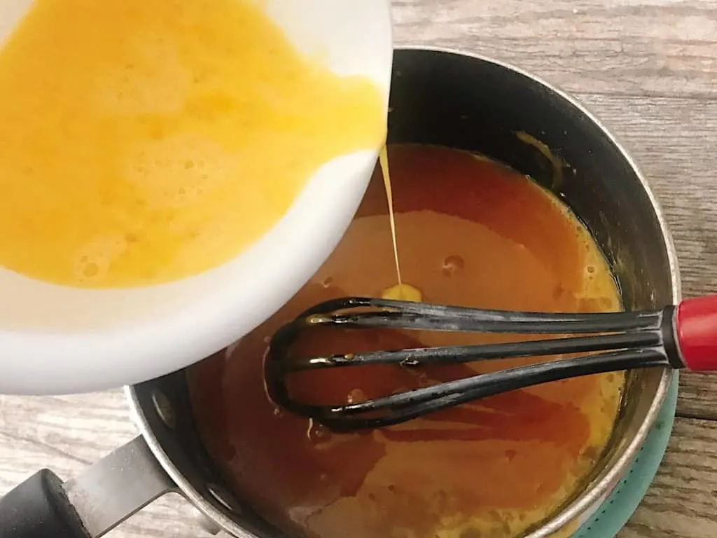 Beaten eggs being poured into a pan of caramel sauce.