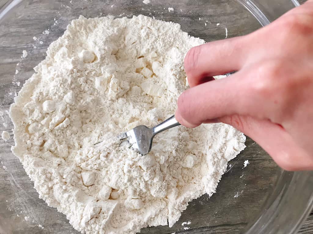 A fork cutting butter into biscuit dough