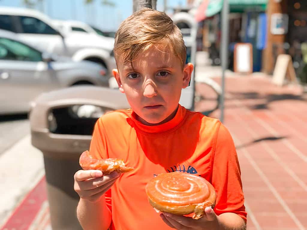 A boy in Newport Beach California eating a cinnamon roll from Seaside Bakery