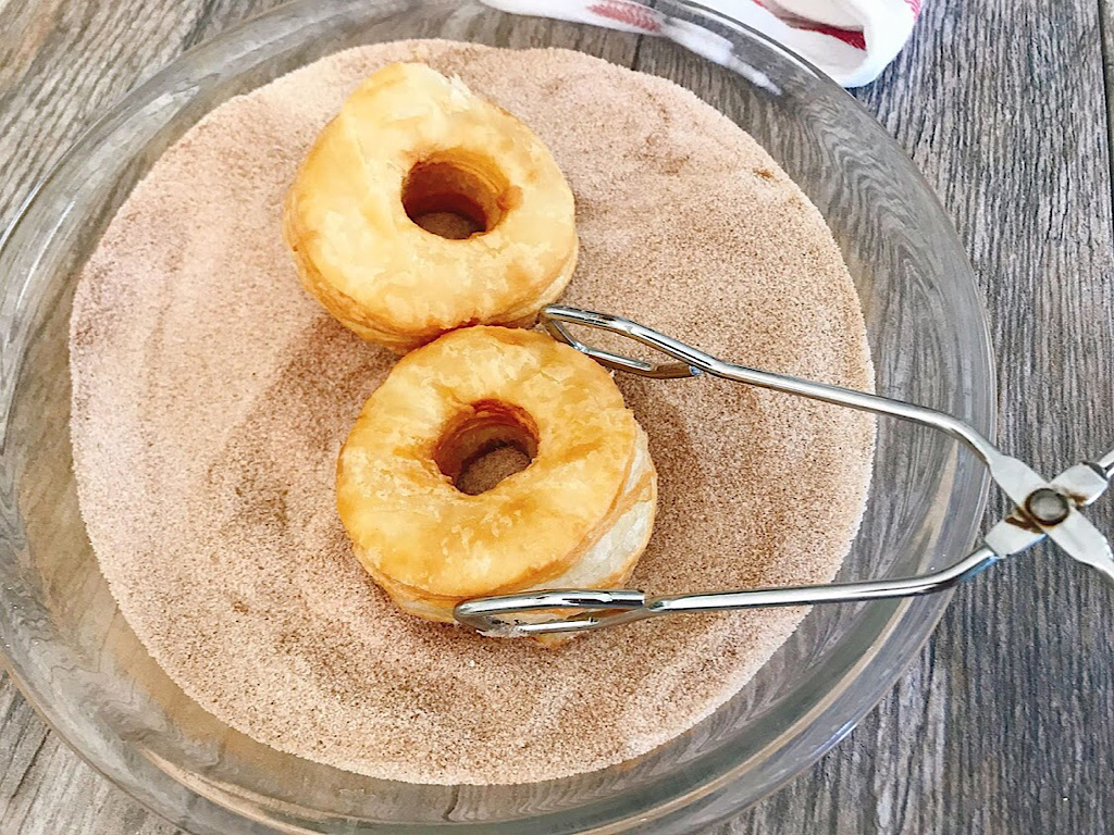 Cronuts being dusted in cinnamon sugar