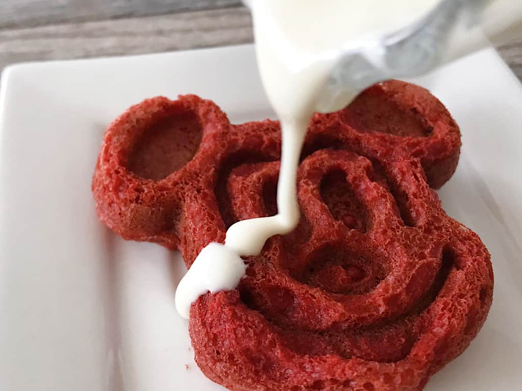 Cream cheese syrup drizzled on a red velvet Mickey waffle