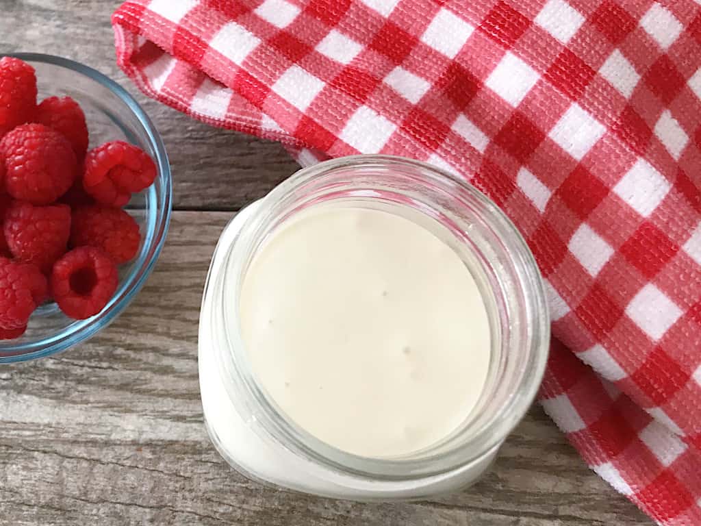 Cream cheese syrup in a mason jar with a kitchen towel and a bowl of raspberries