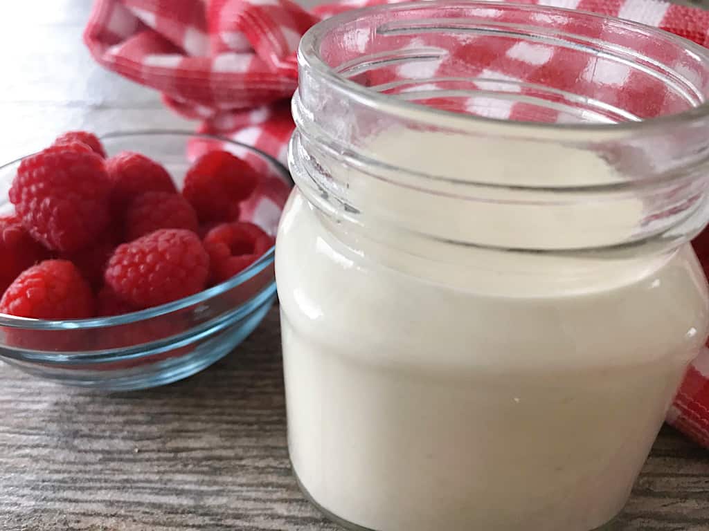 Cream cheese glaze in a jar next to a bowl of raspberries
