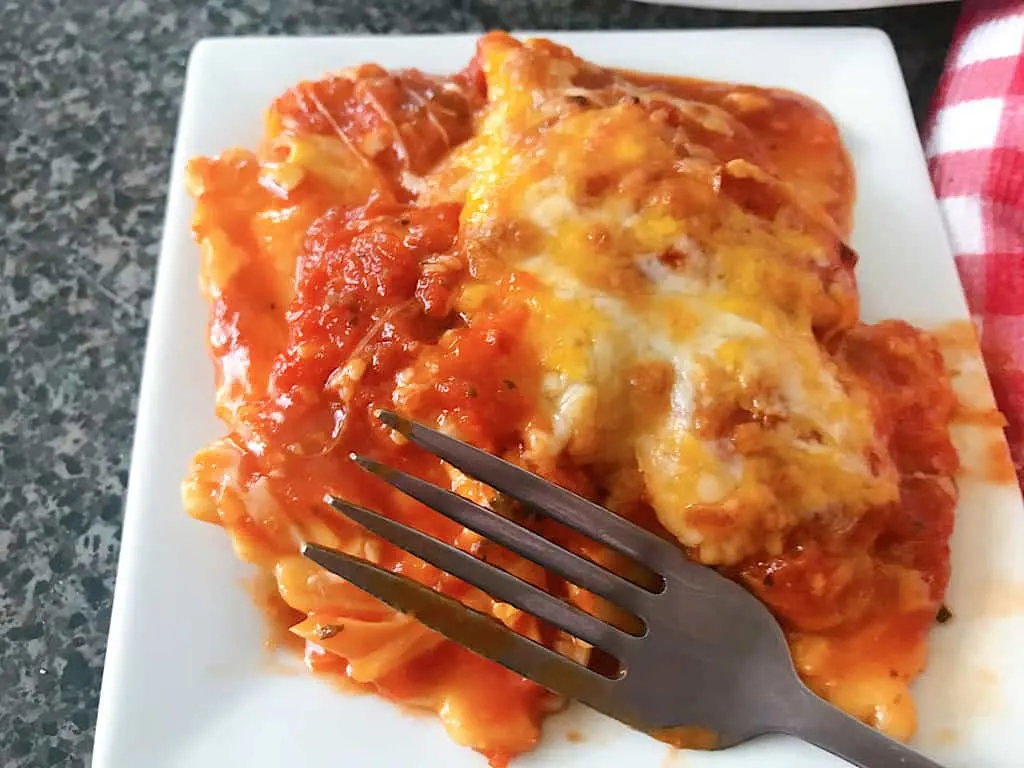 A plate with ravioli, sauce, cheese, and a fork.