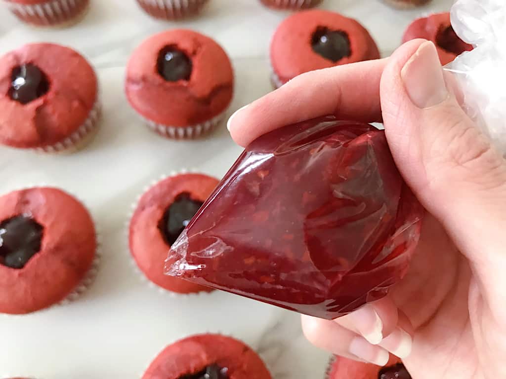 Add the raspberry preserves to a ziplock bag, and pipe filling into each cupcake hole.