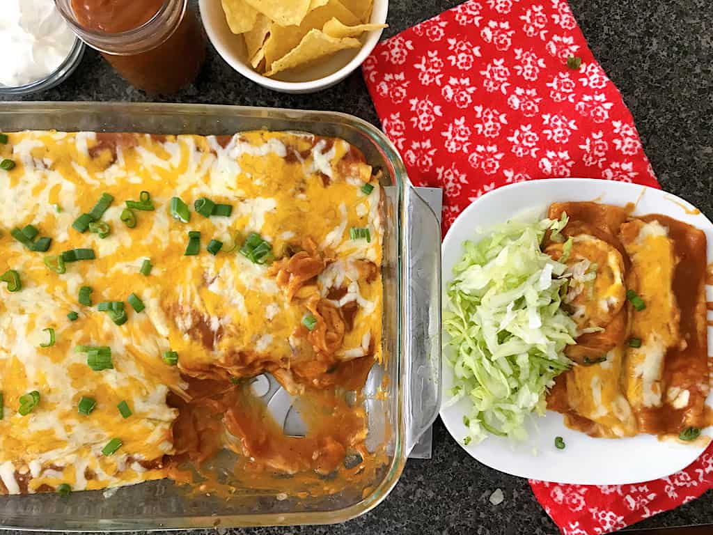 A pan of cheese enchiladas, with a plate of enchiladas