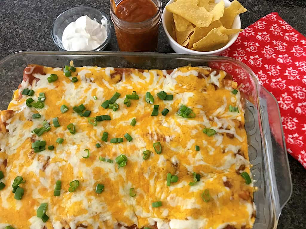 A pan of cheese enchiladas, a bowl of tortilla chips and sour cream