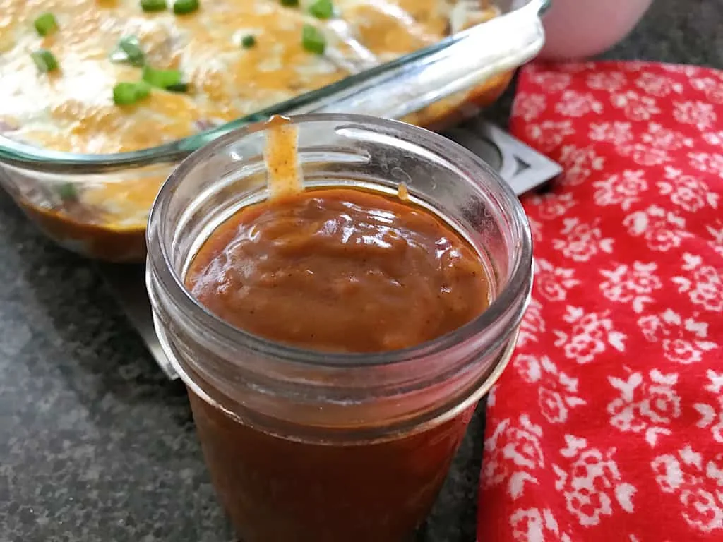 A jar of homemade enchilada sauce and a pan of cheese enchiladas