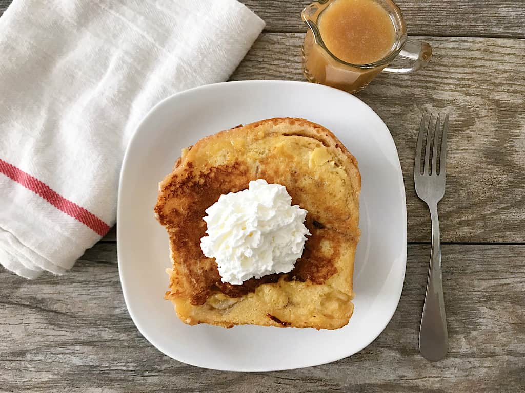 Chunky Cinnamon French Toast with whipped cream and a cup of caramel syrup