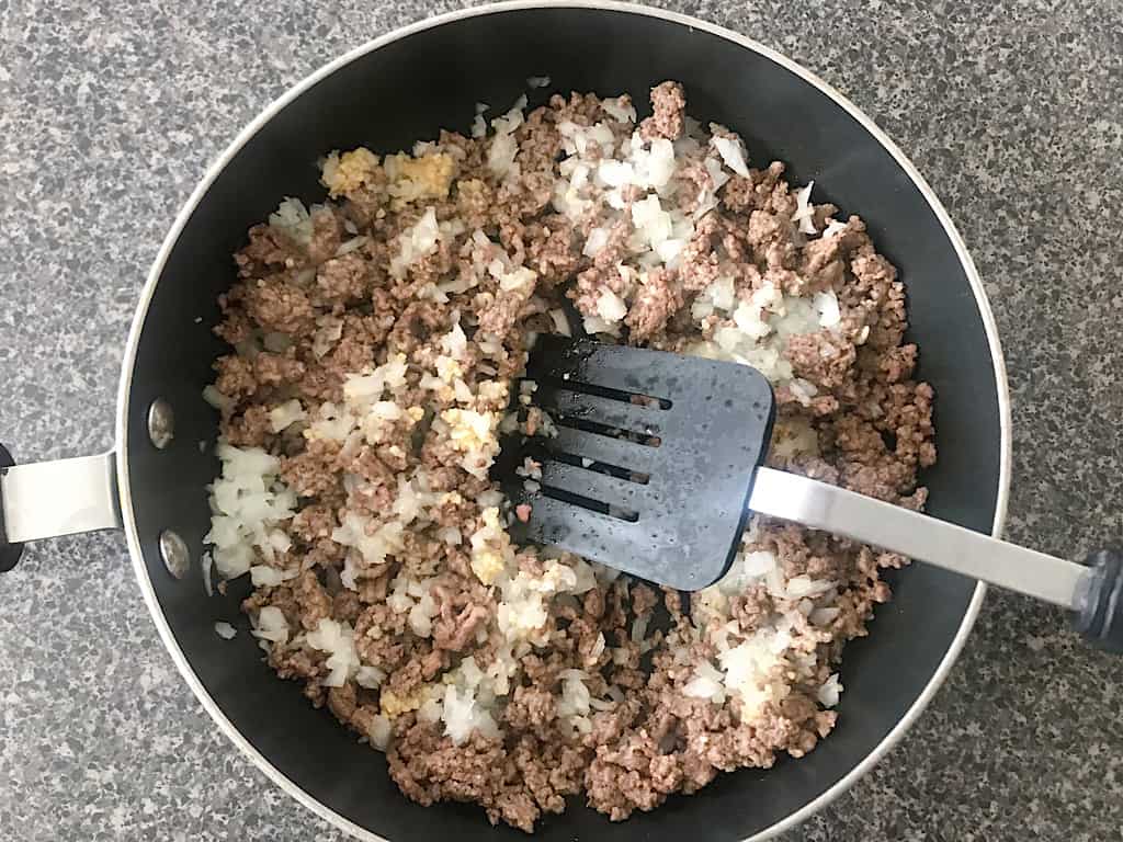 Add the chopped onions and minced garlic to the meat and continue to cook for about 5 minutes until the onions begin to soften and become translucent.