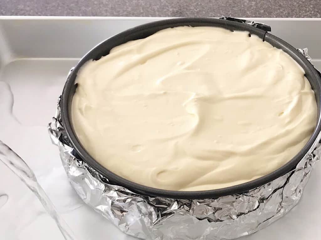 Cheesecake batter in a springform pan, placed in a roasting pan being filled with water.