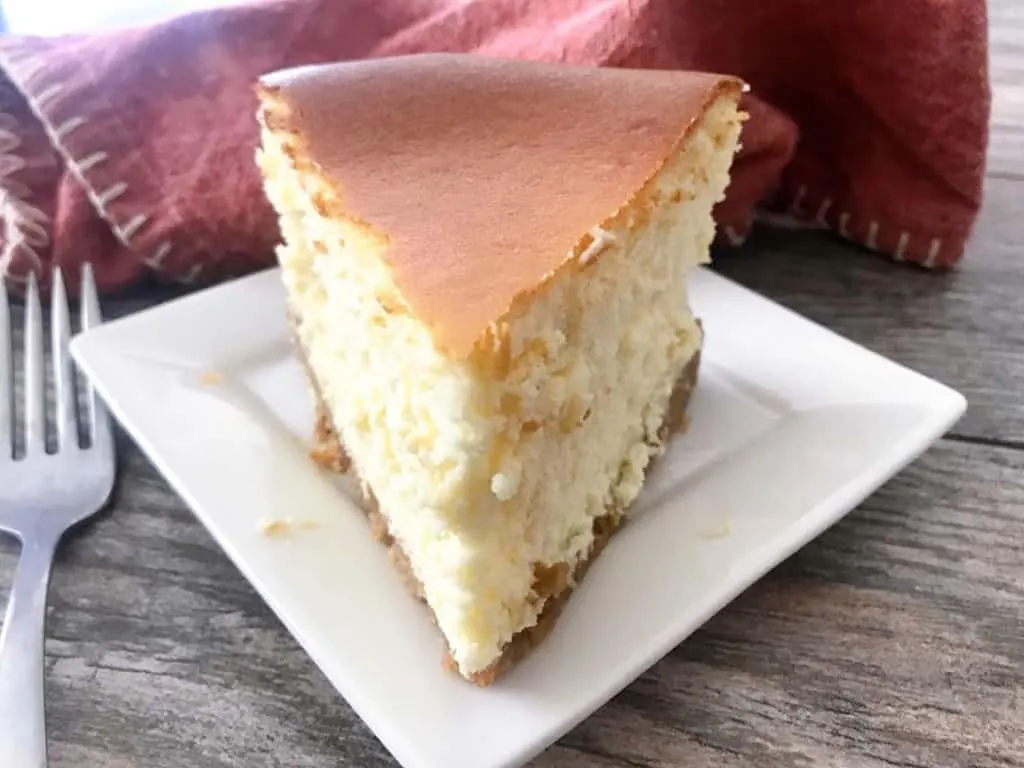 A slice o New York Cheesecake on a white plate.
