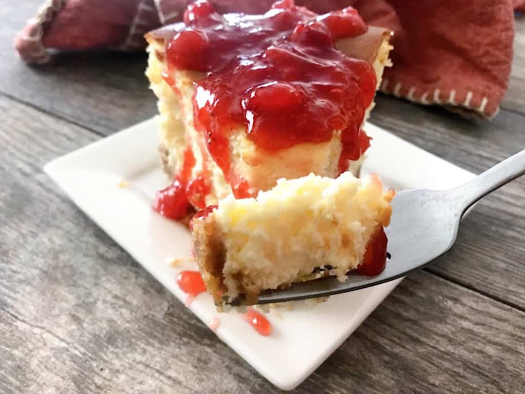 A bite of cheesecake with strawberry syrup