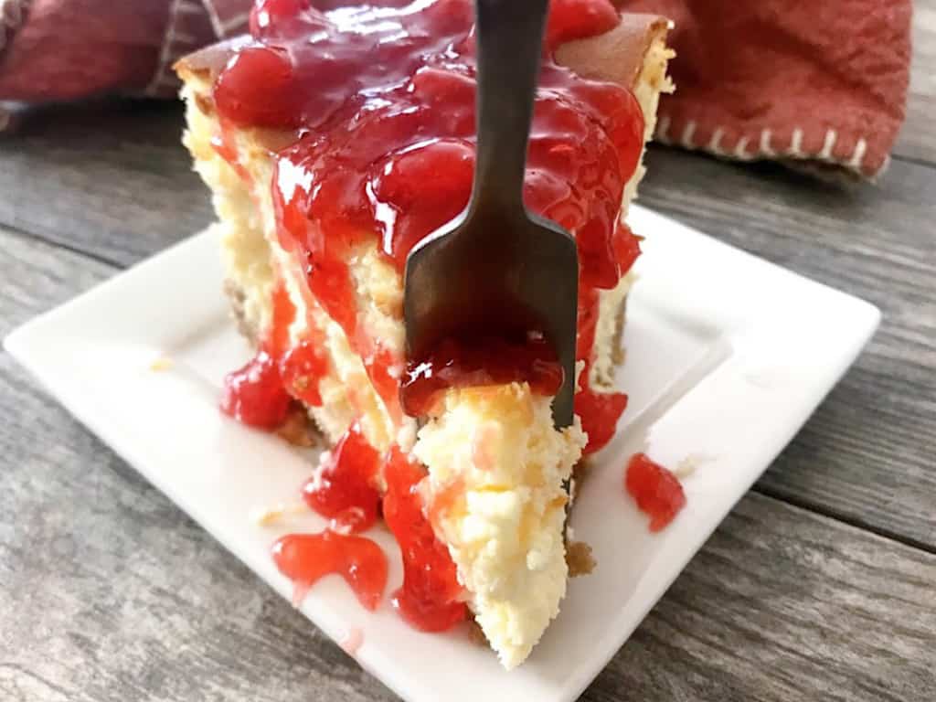 A fork in a slice of classic New York cheesecake topped with strawberries.