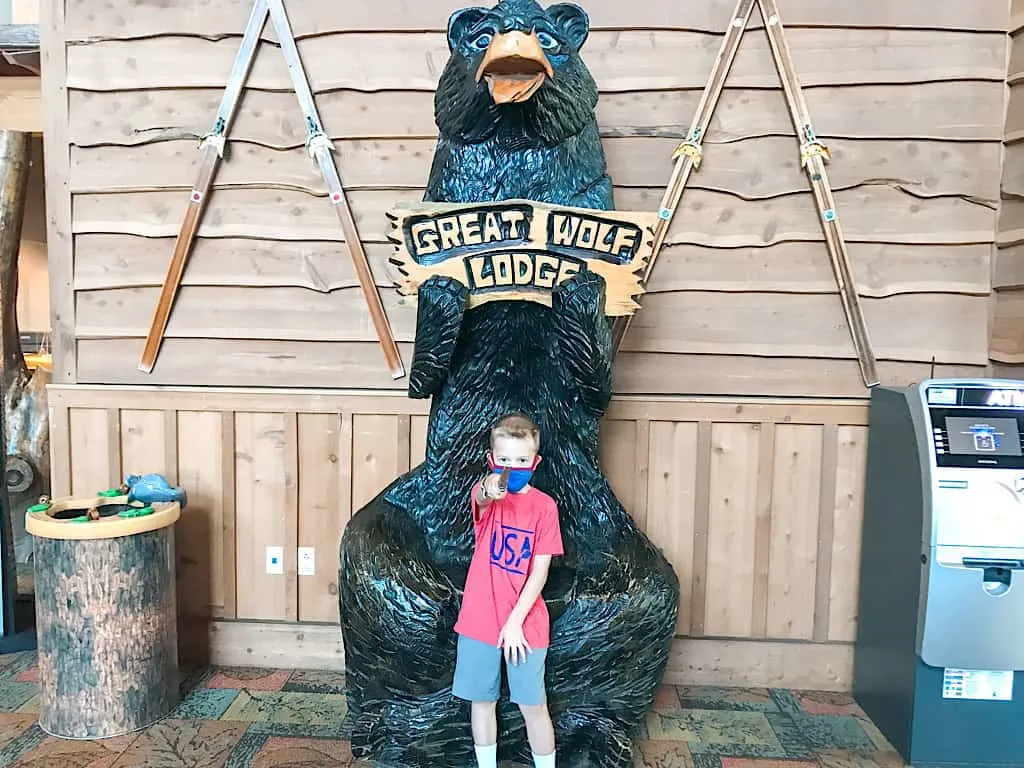 A child in front of a wooden bear with a sign that says Great Wolf Lodge