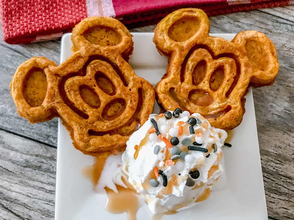 Two Pumpkin spice Mickey waffles with a scoop of ice cream and sprinkles.