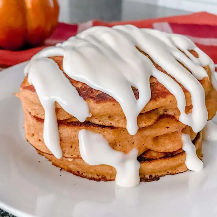 A stack of pumpkin pancakes covered in cream cheese syrup.