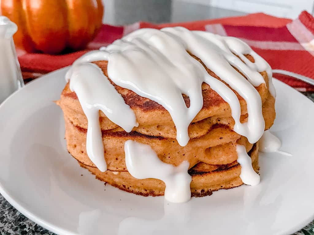 A stack of pumpkin pancakes covered in cream cheese syrup.
