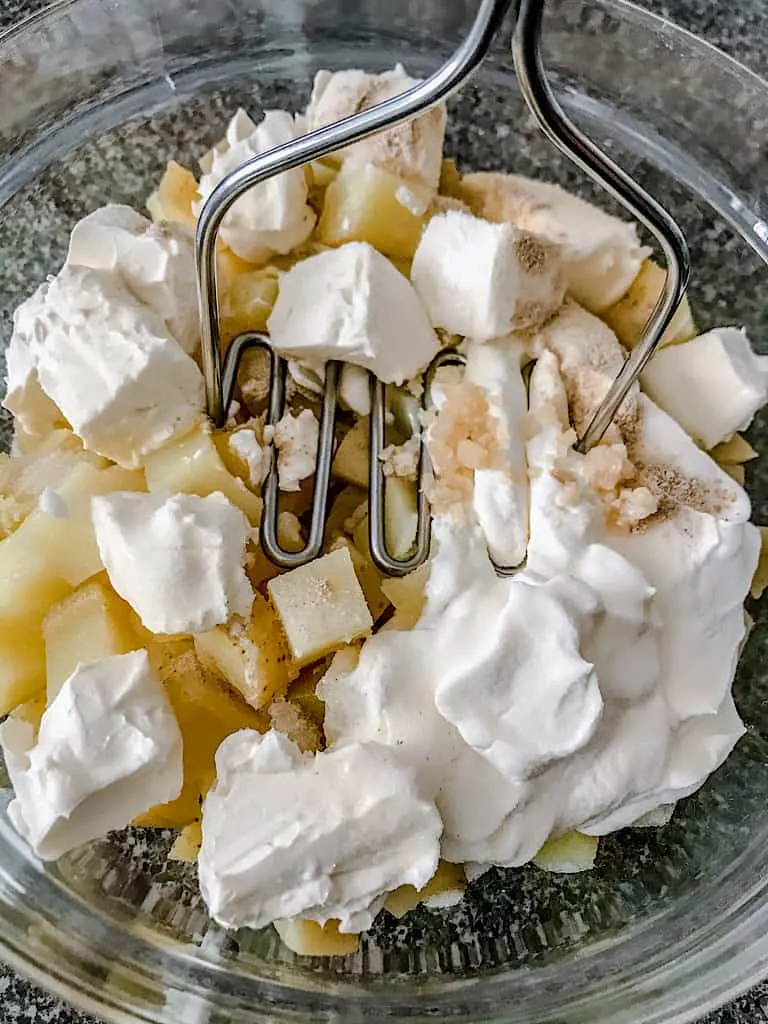 Add butter, sour cream, cream cheese, garlic, salt, and white pepper to the potatoes.