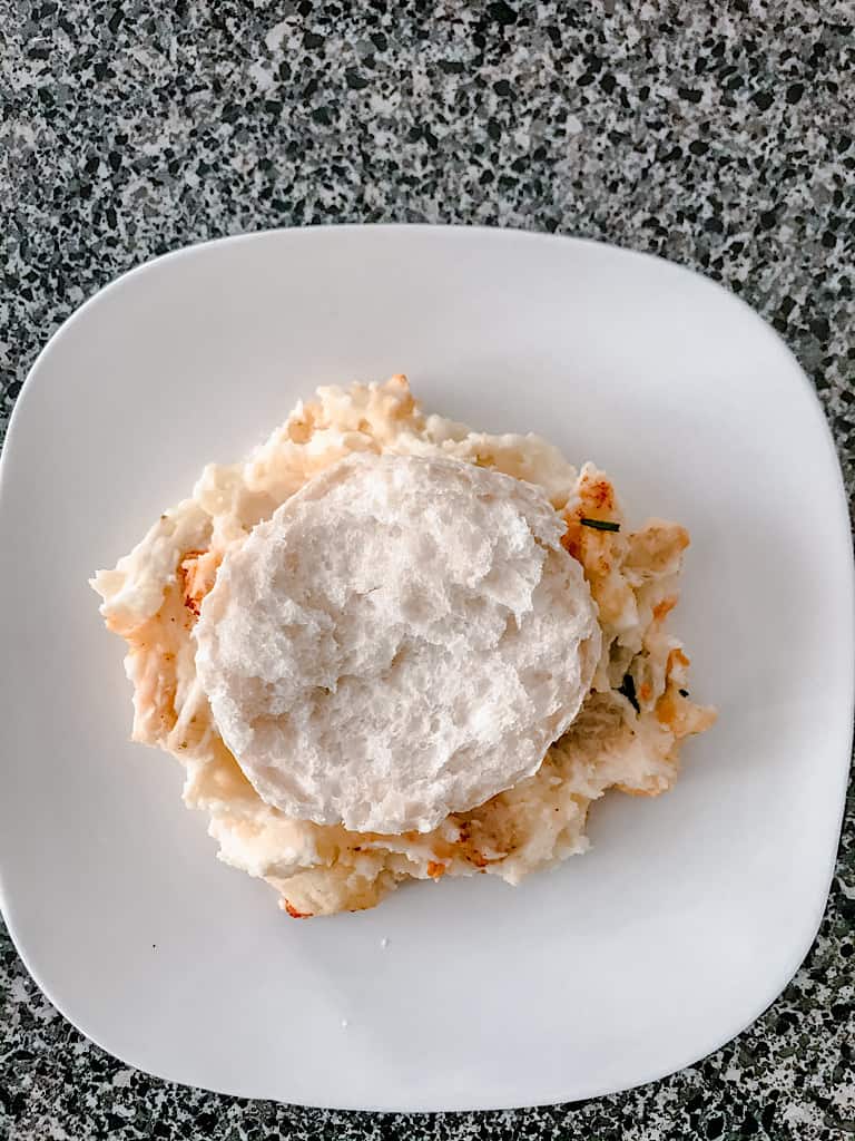 A biscuit on a plate of mashed potatoes.