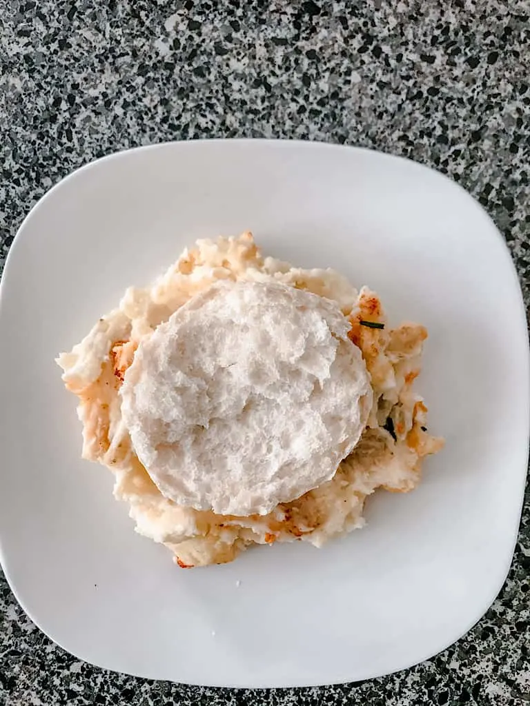 A biscuit on a plate of mashed potatoes.
