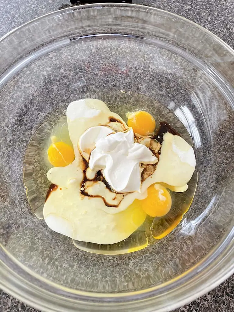 In a large mixing bowl, whisk together the eggs, milk or buttermilk, oil, sour cream, and vanilla extract.