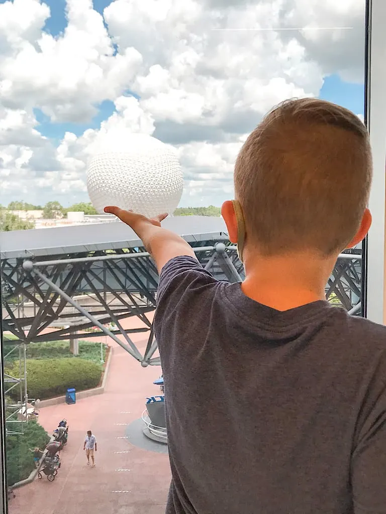 A boy holding out his arm which looks like it is holding up Spaceship Earth at Epcot