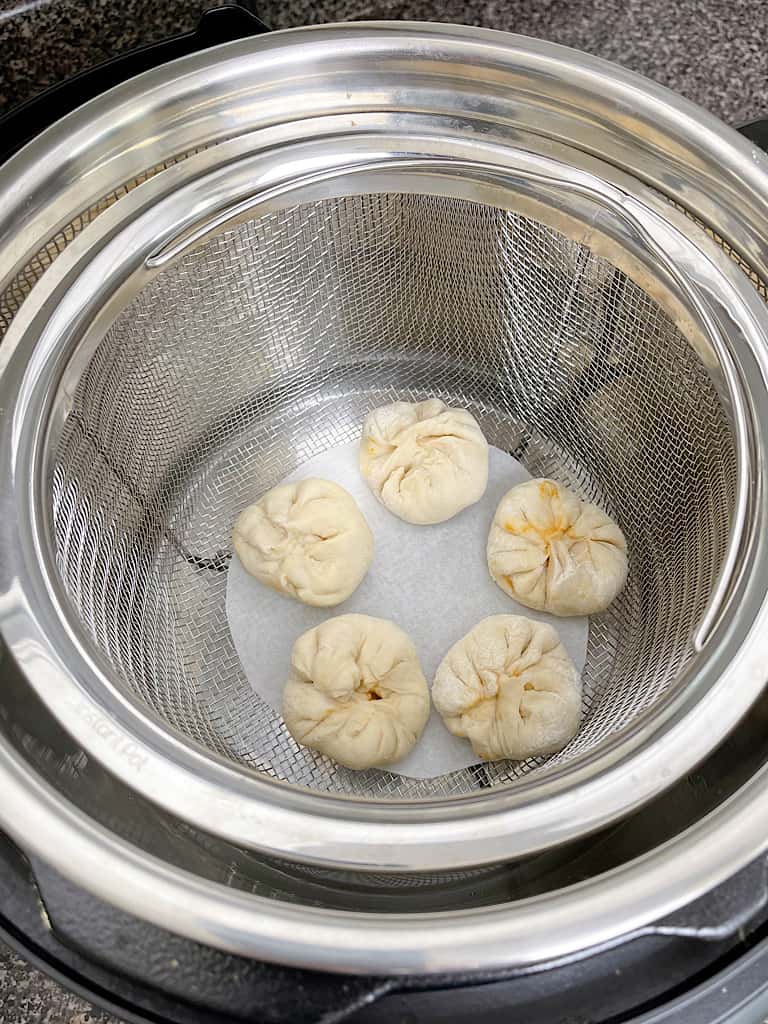 Water in an instant pot with a steamer basket and bao buns.
