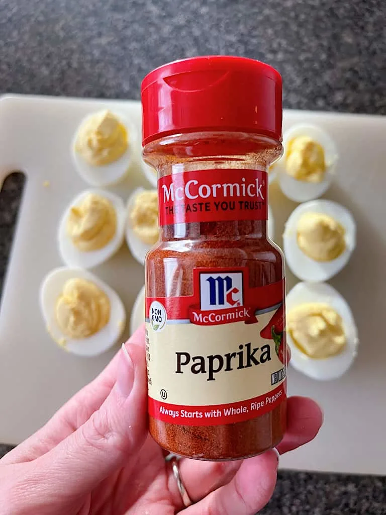 A jar of paprika held over bacon ranch deviled eggs.