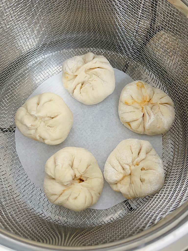 Homemade cheeseburger pods on parchment paper in an Instant Pot steamer basket.