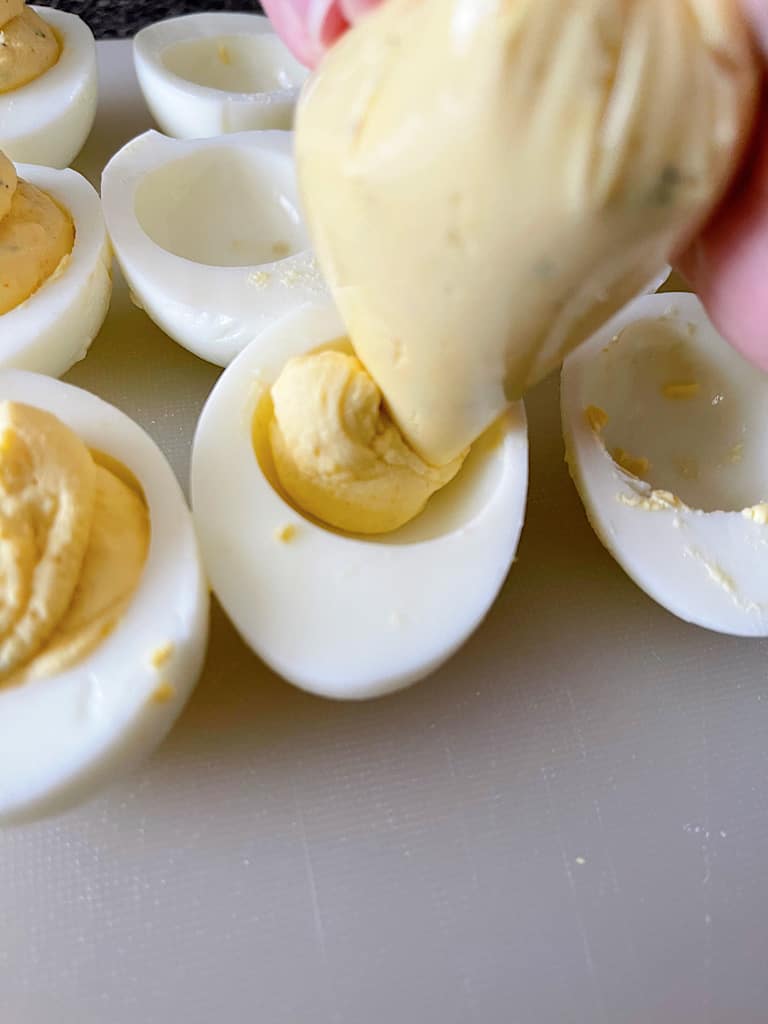 Deviled Egg filling being piped into egg white halves.