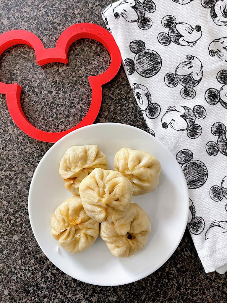 Cheeseburger pods on a white plate with a red Mickey Mouse cookie cutter and a Mickey kitchen towel.