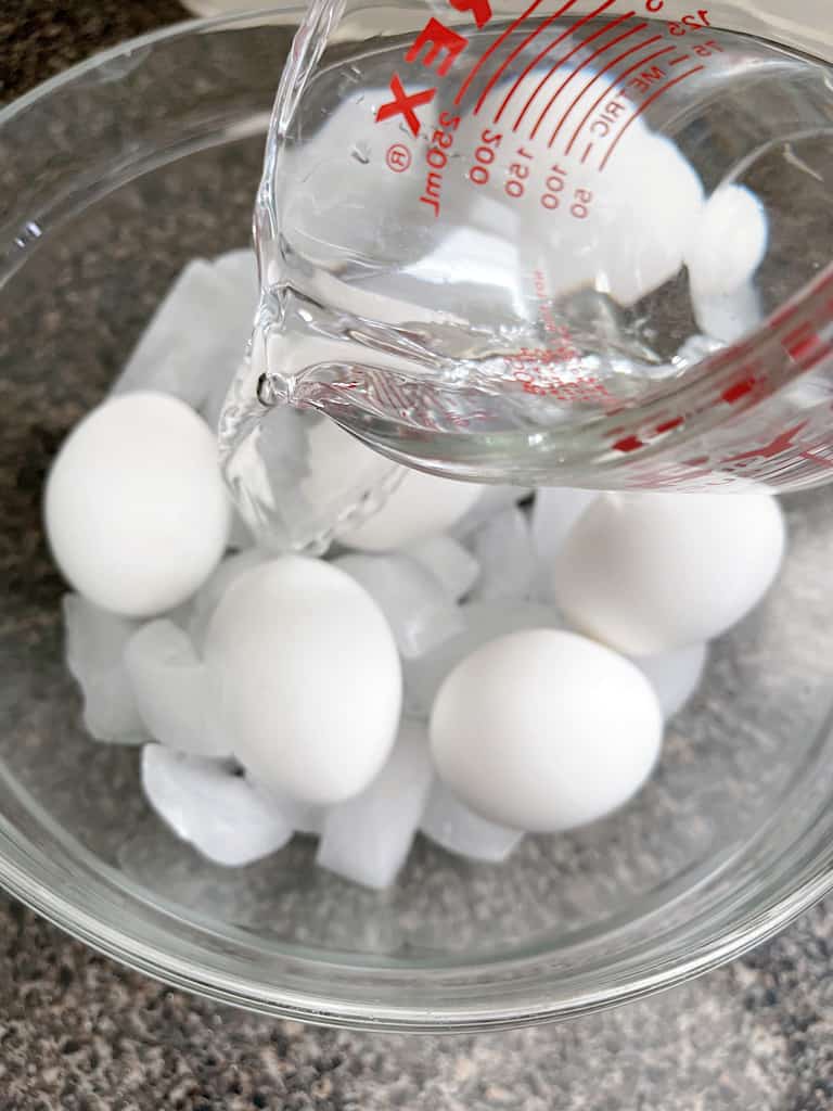 Water in a measuring cup being poured over a bowl of eggs.