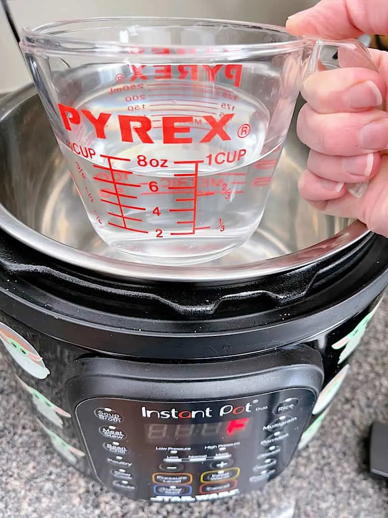 Water in a measuring cup held over an Instant Pot.
