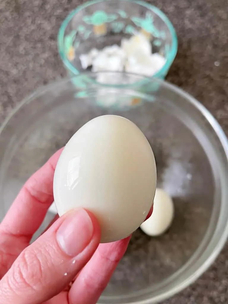 A hand holding up a peeled, hard boiled egg.